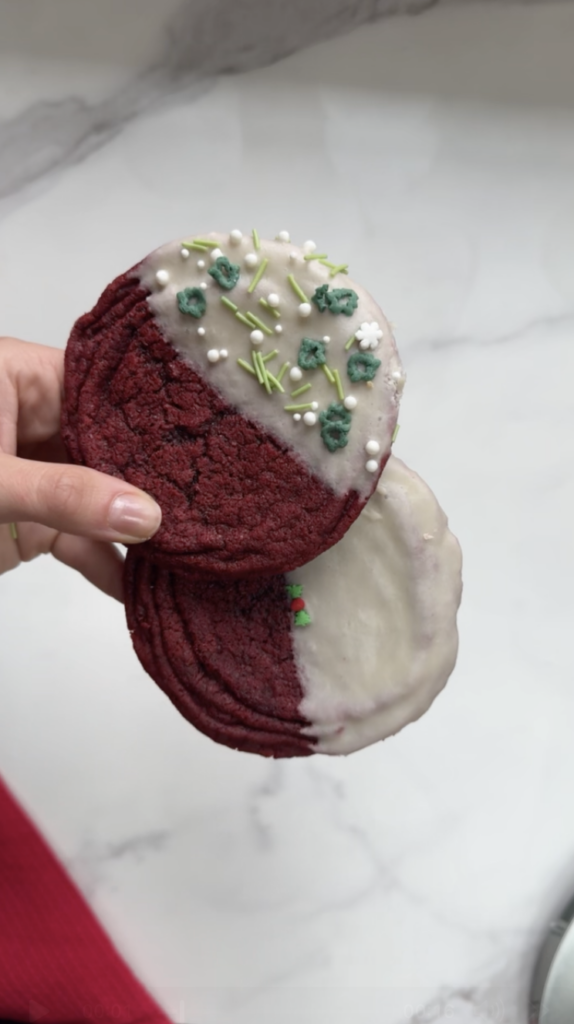 Two red velvet cookies with cream cheese glaze being held in one hand